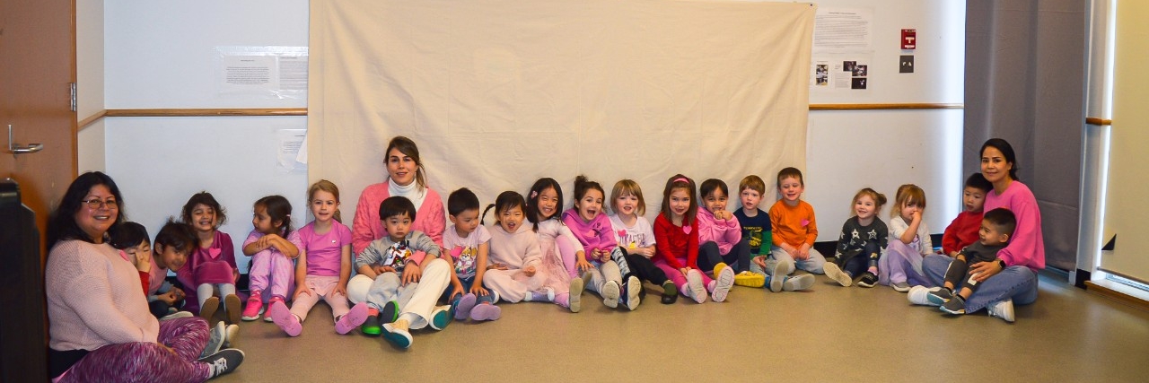 Picture is of staff members sitting in a semi-circle with children from SFU childcare. There is a staff member sitting on both ends as well as one in the middle.
