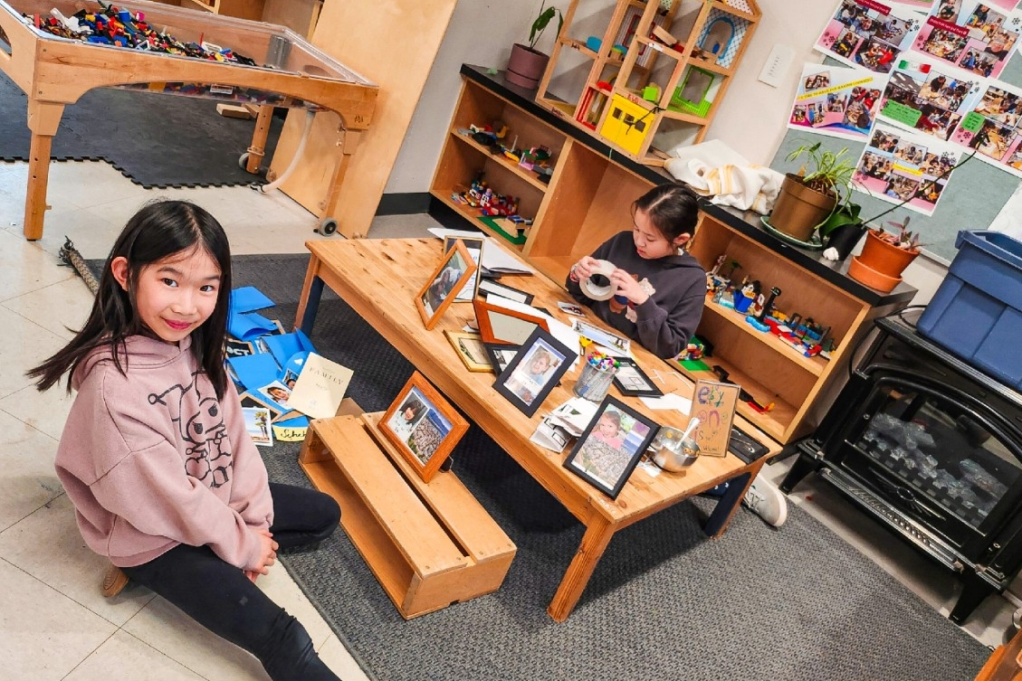two children in school aged program. One child is smiling and facing the camera while the other child is working on so educational crafts at the table