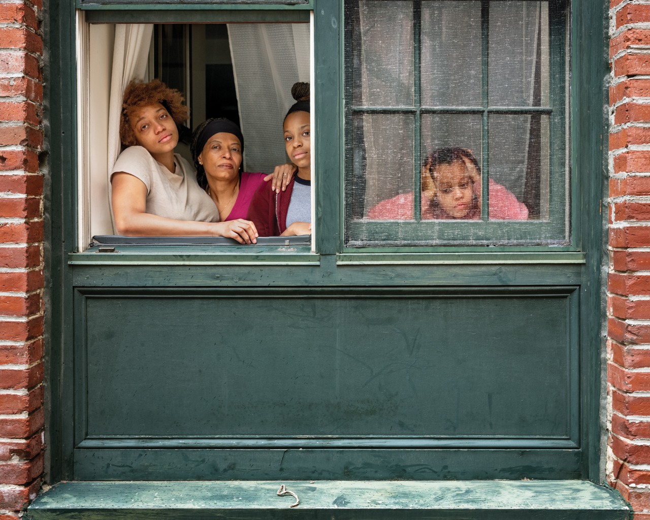 Figure 1. “Minty, Kayla, Leyah, Layla, Cambridge Massachusetts, 2020.” Family members, Minty, Kayla, Leyah, Layla, physically lean on each other as they look through their window.