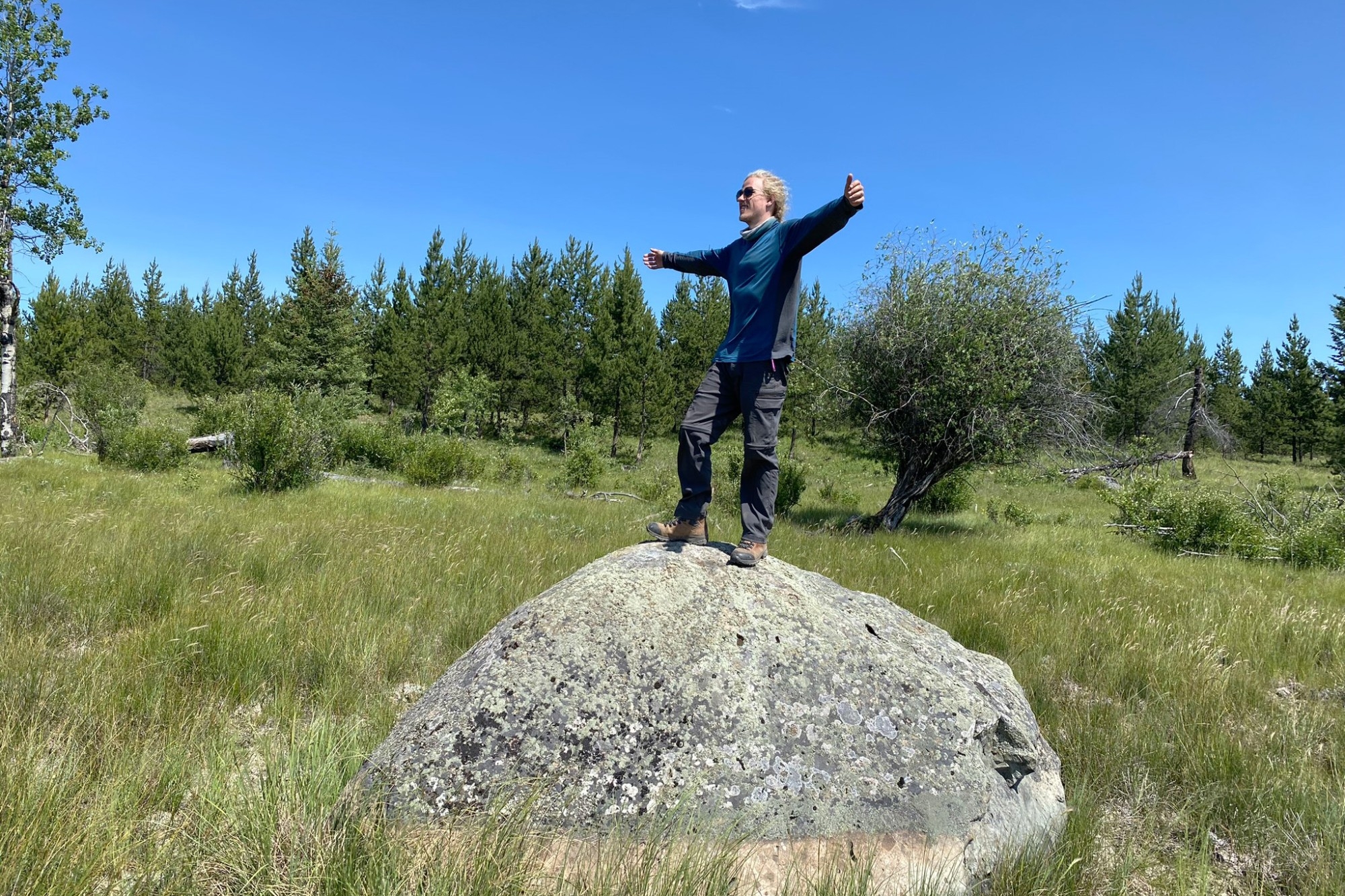 Matthew standing on a large rock with arms outstretched