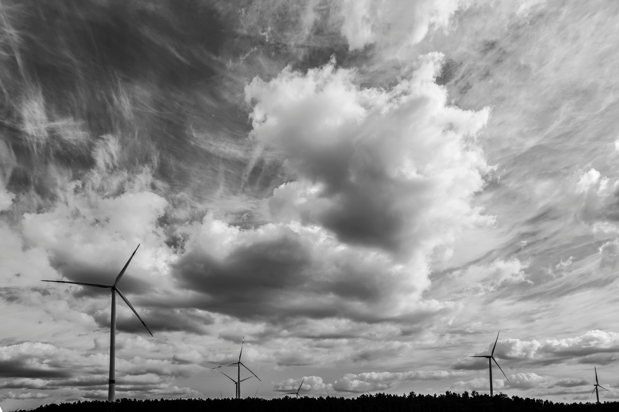 Grayscale photo of wind turbines under cloudy sky