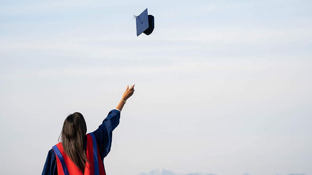 A graduate in regalia throwing her cap in the air in celebration