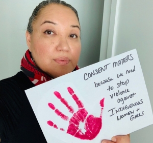 Woman holding a paper sign that reads: “Consent Matters because - we need to stop violence against Indigenous Women and Girls.”  Indigenous women’s are 3.5 times more likely to experience violence than non-Indigenous women and homicide rates of Indigenous women are 7 times higher than non-Indigenous women (Native Women’s Association of Canada Fact Sheet)