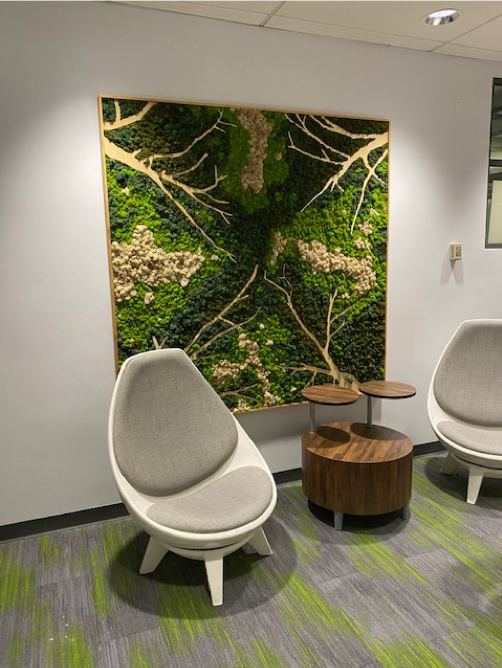 A grey chair sits in front of a wall with a mossy design in different shades of green.