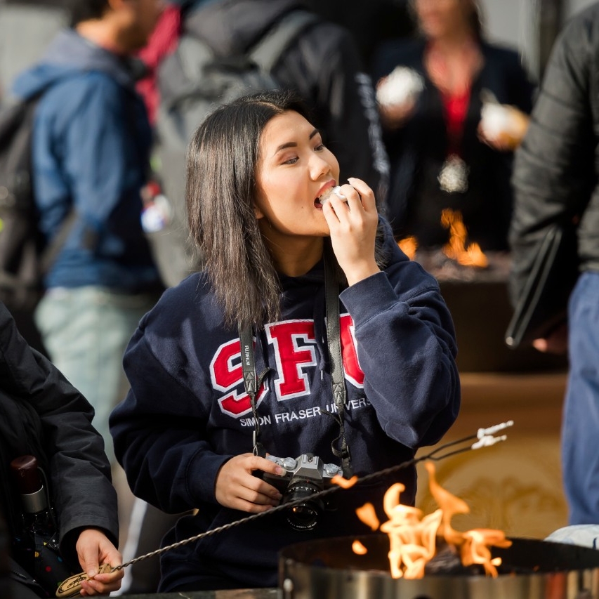 An SFU student sitting at a fire pit and eating marshmallows