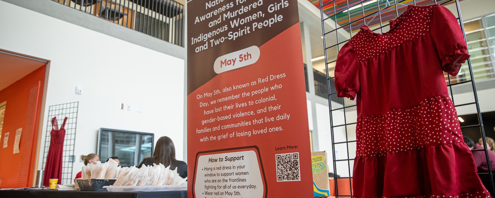 red dress hanging beside a National Day of Awareness for MMIWG2S banner
