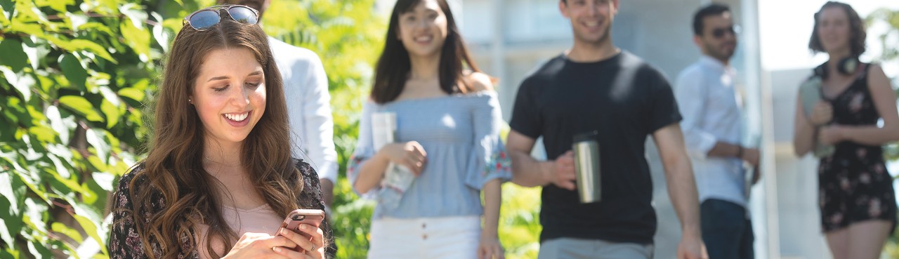 SFU resident looking and her phone and smiling outside townhouses. 