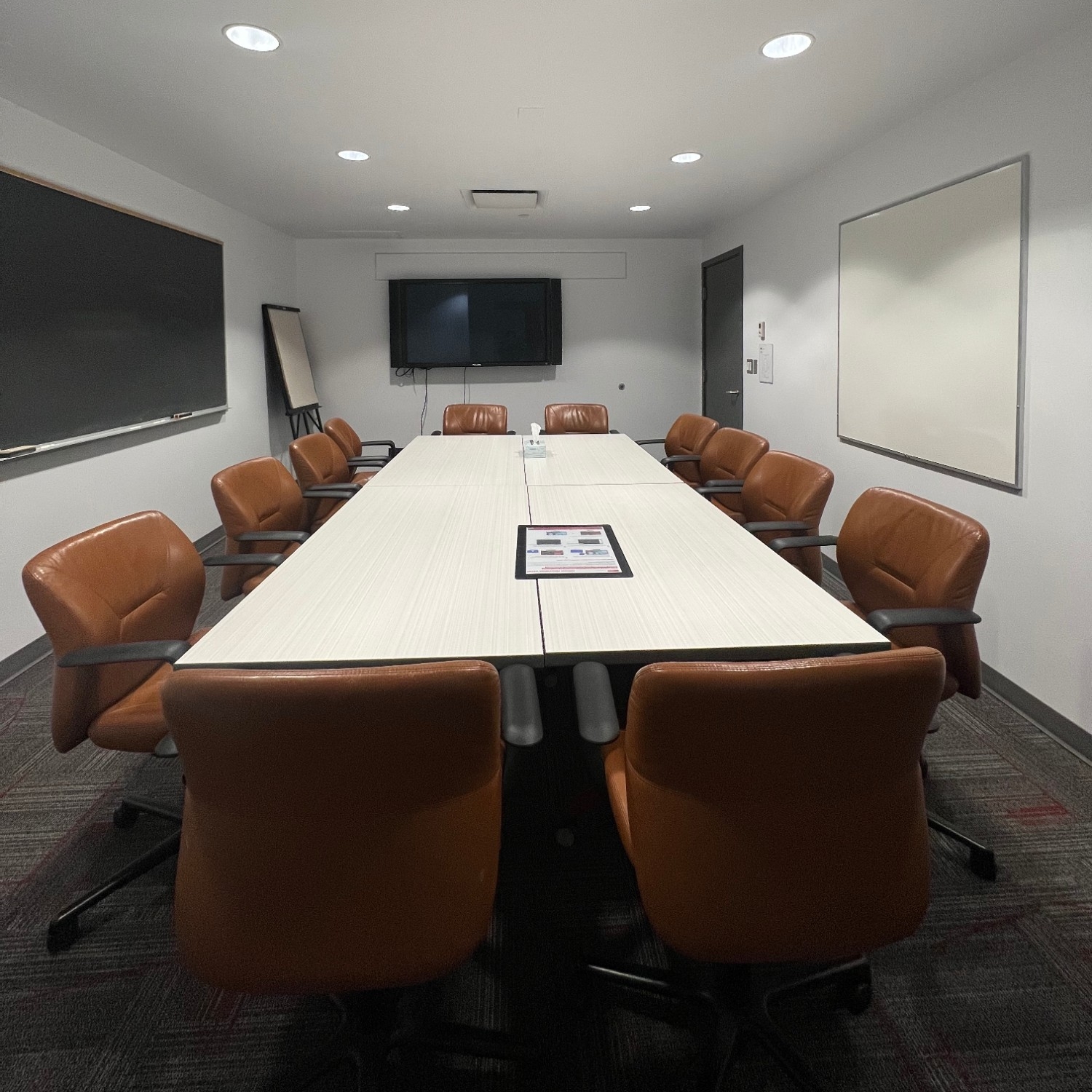 Small, enclosed meeting space with table, chairs, whiteboard, chalkboard, and monitor