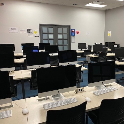 Enclosed lab space with rows of desktop computers on tables with chairs