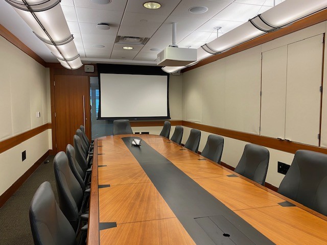 Enclosed space with large boardroom style table, chairs, and projector screen