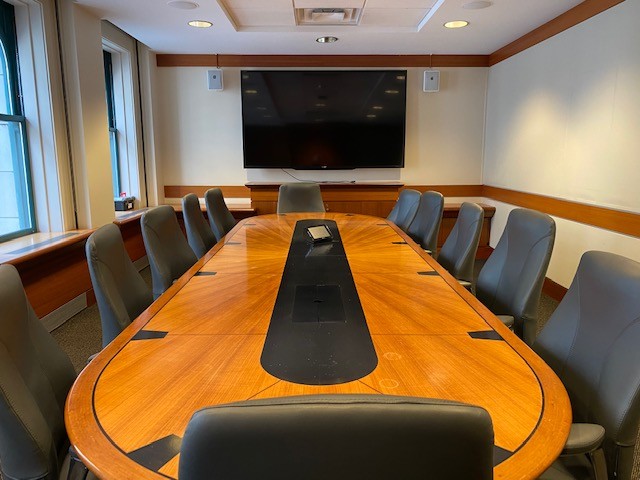 Enclosed space with large boardroom style table, chairs, and video screen