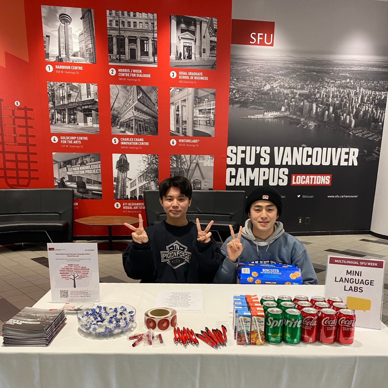 Two students sitting at a table and giving away snacks and prizes as part of an activity for Multilingual Week 2023 at Vancouver campus