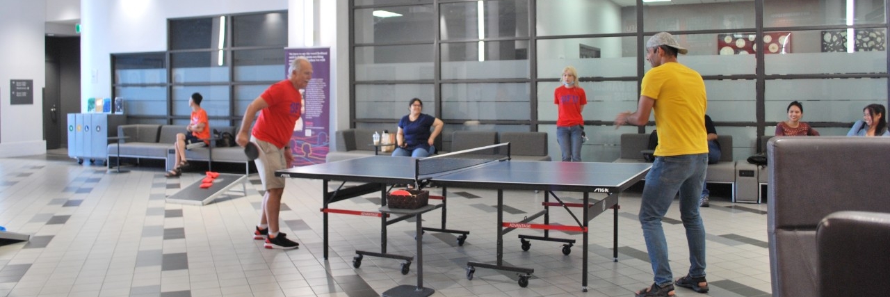 Two people playing ping pong, with a few other people watching