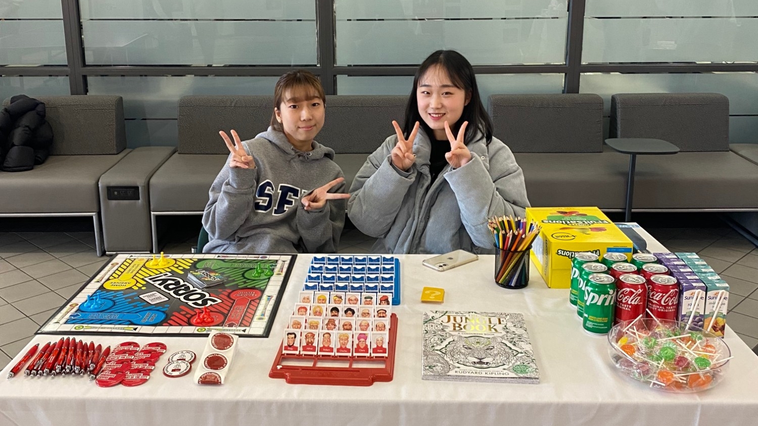 Two students sitting at a table and giving away snacks and prizes as part of a board games activity for Multilingual Week 2023 at Vancouver campus