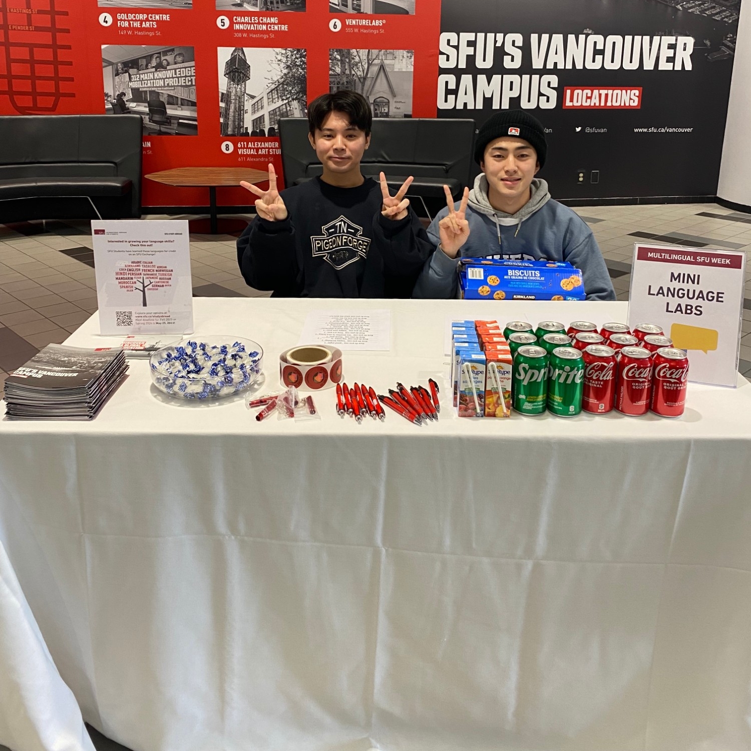 Two students sitting at a table and giving away snacks and prizes as part of a mini language labs activity for Multilingual Week 2023 at Vancouver campus