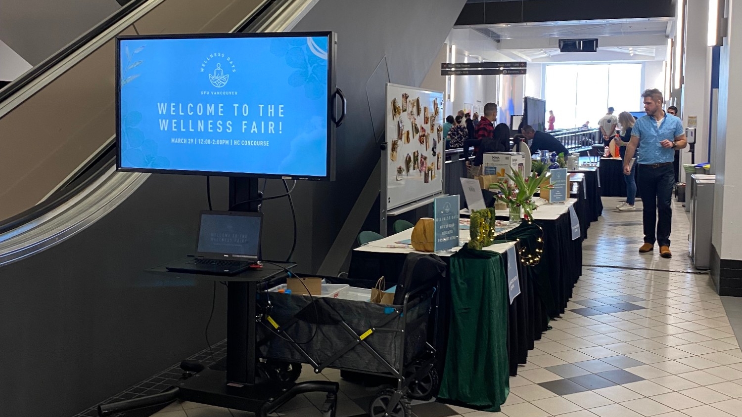 A monitor reading "Welcome to the Wellness Fair!" with multiple tables and people in the background at Wellness Fair, as part of 2023 Wellness Days