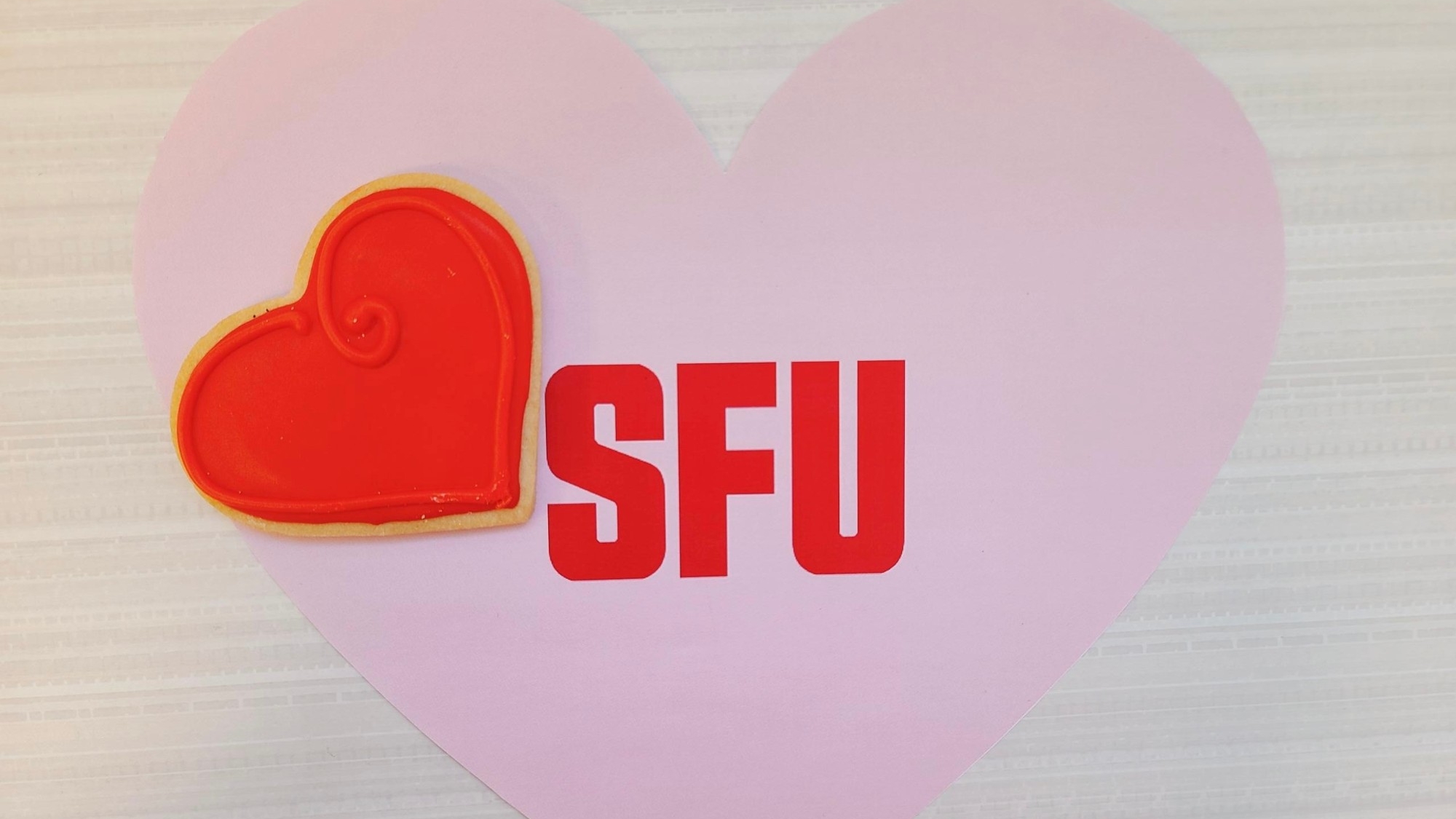 Heart-shaped cookie on top of a pink heart-shaped SFU sign