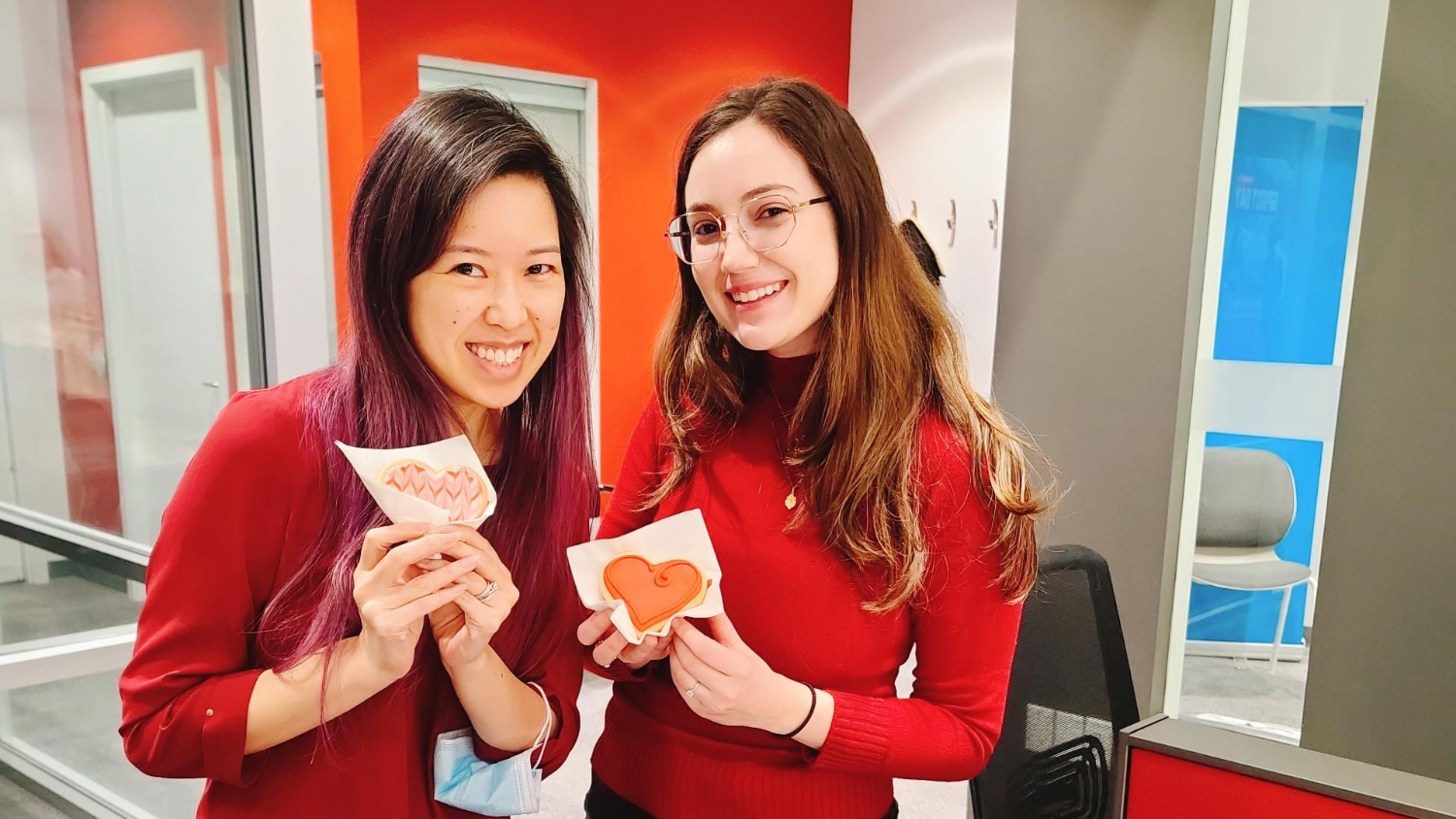Two staff members holding up heart-shaped cookies 