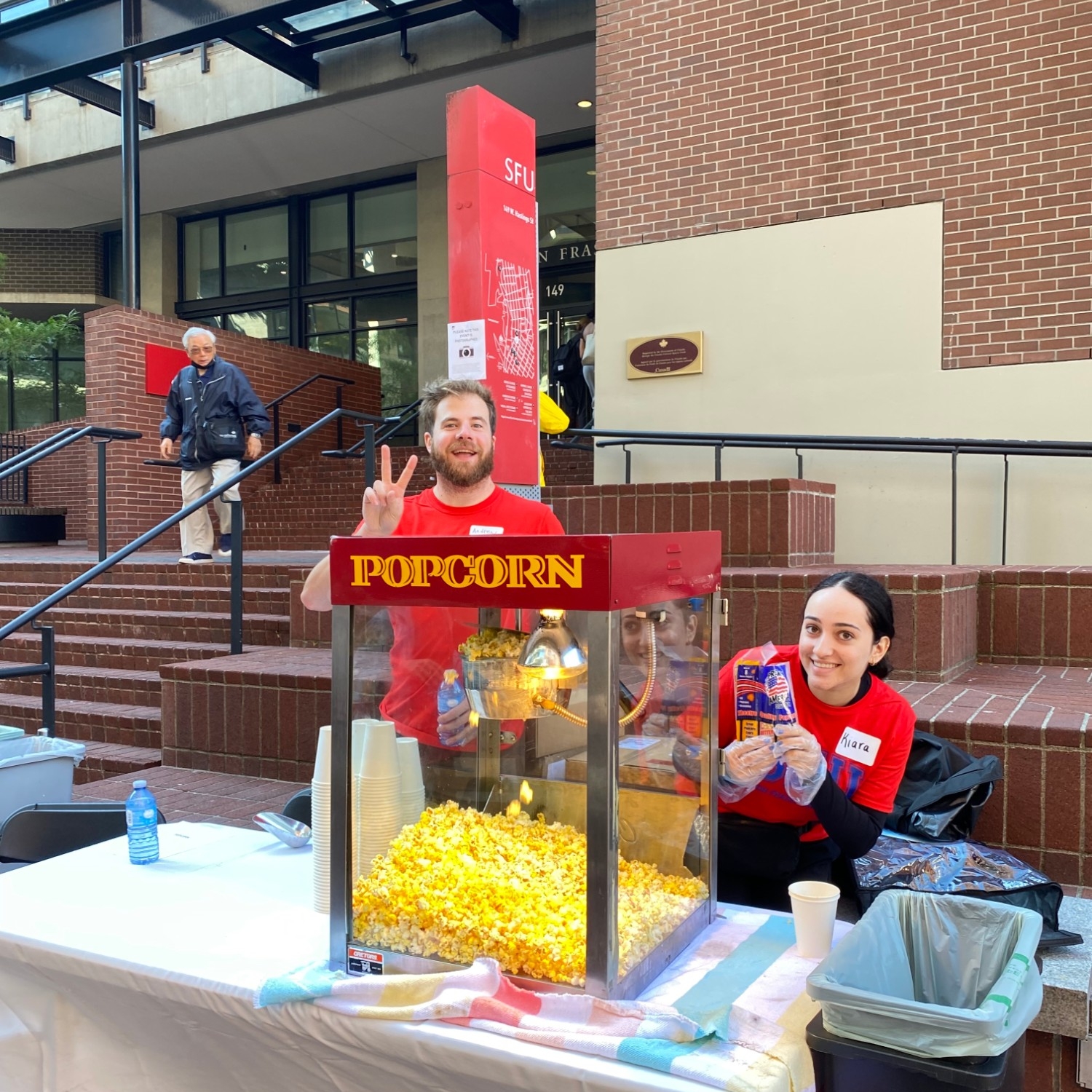 A staff member and co-op student volunteering at the popcorn machine during the 2023 SFU Vancouver Welcome Back Community BBQ in the Woodward's Atrium