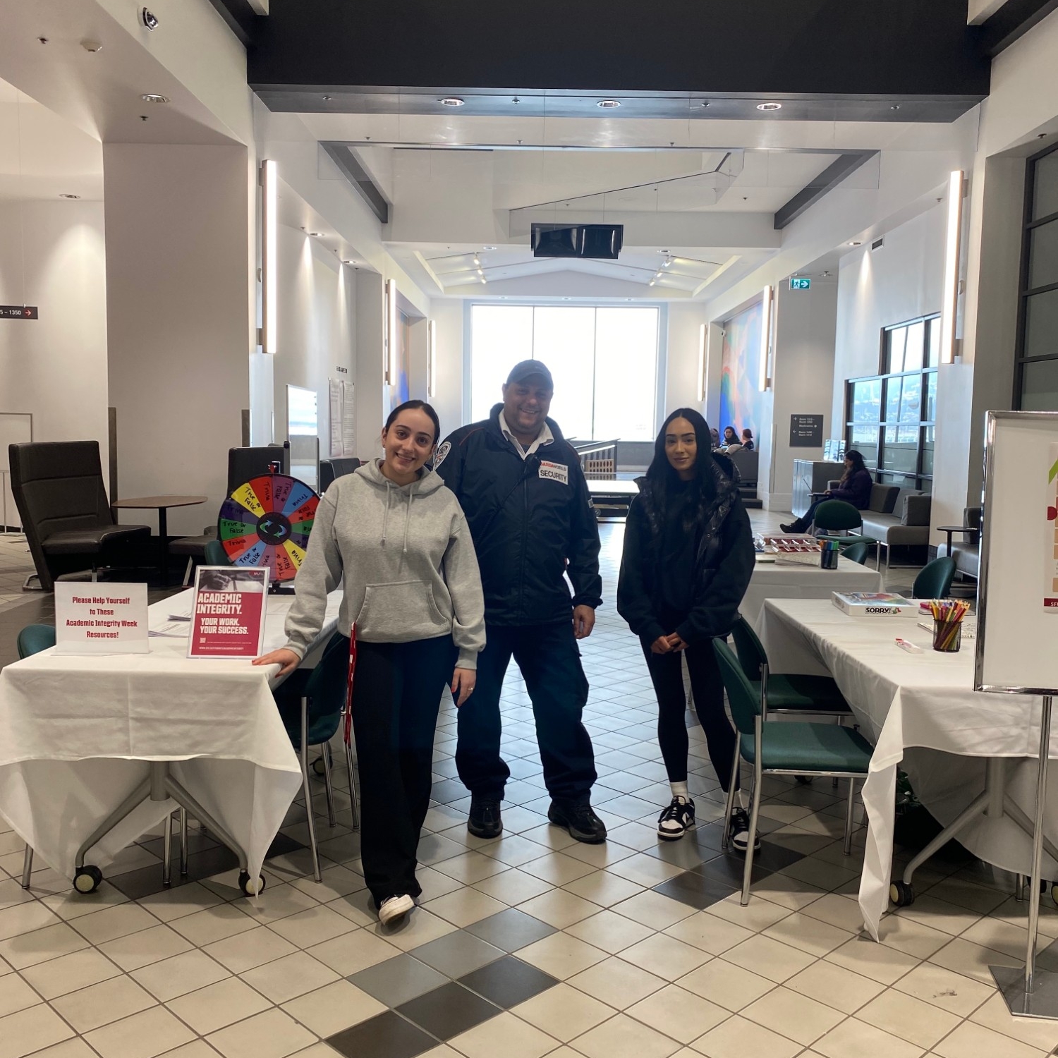 Two student-staff members and a Campus Public Safety team member at a 2023 Academic Integrity Week event in the Harbour Centre Concourse
