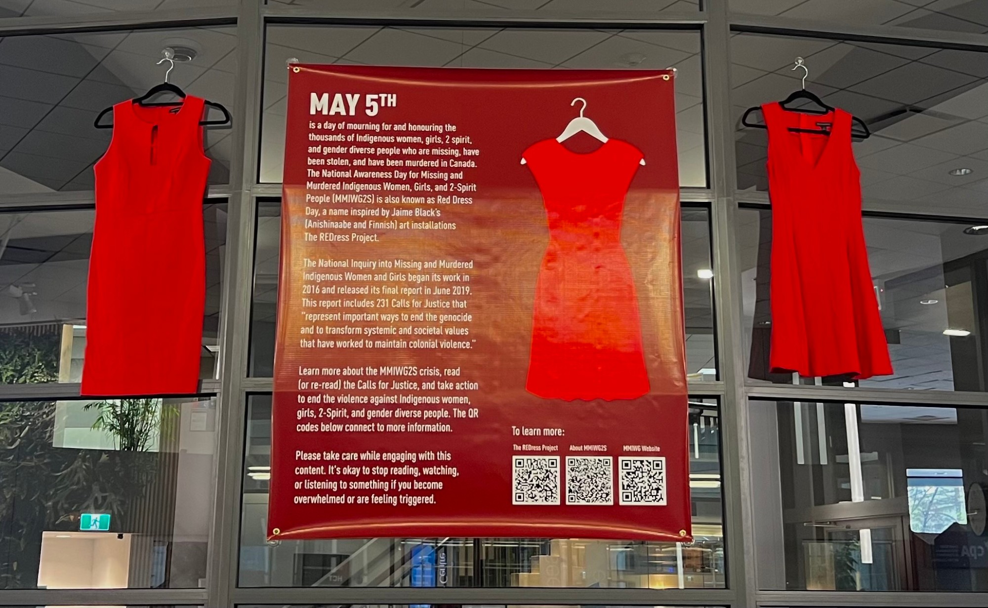Two red dresses and a poster hanging on the windows of the Belzberg Library as a display for 2023 Red Dress Day