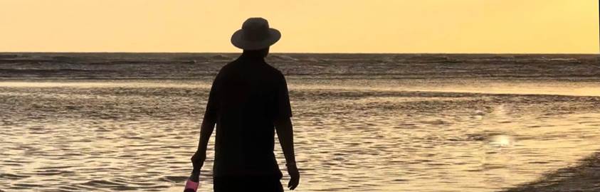 A person in a hat walking on a beach
Description automatically generated