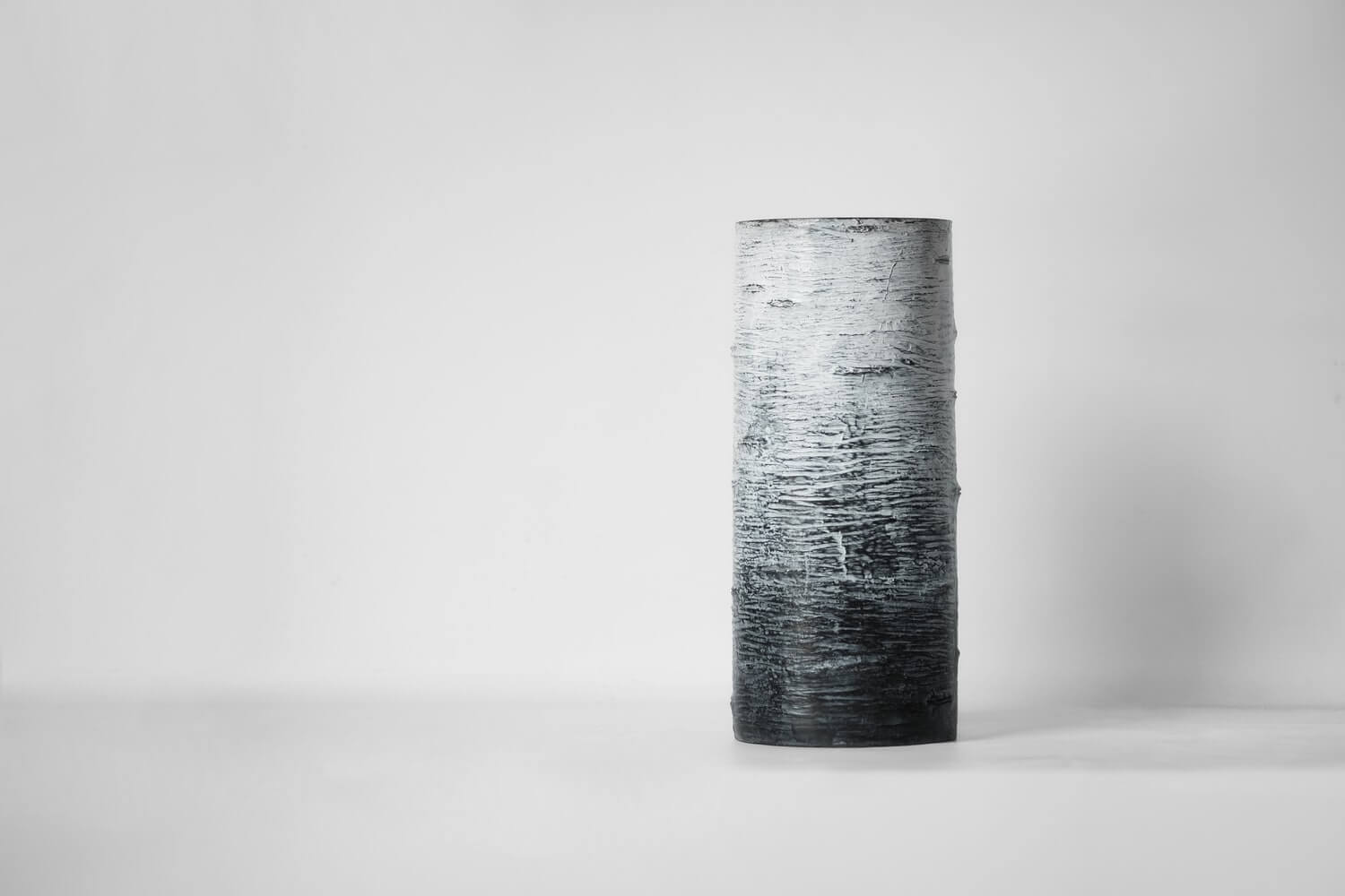 A textured cylindrical vase that has a gradient with white from the top transitioning to black.