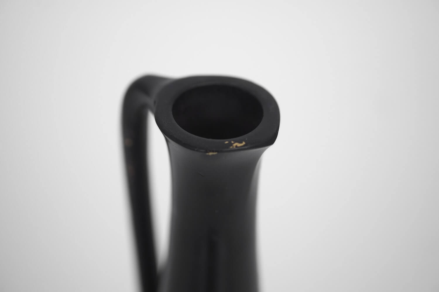 The mouth of a black vase with a gold patina.