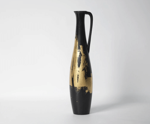 A tall skinny black vase with a handle and gold patina.