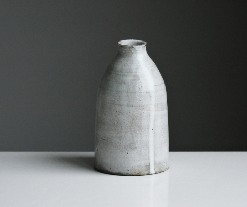 A wide white vase with a skinny neck and grey specks.