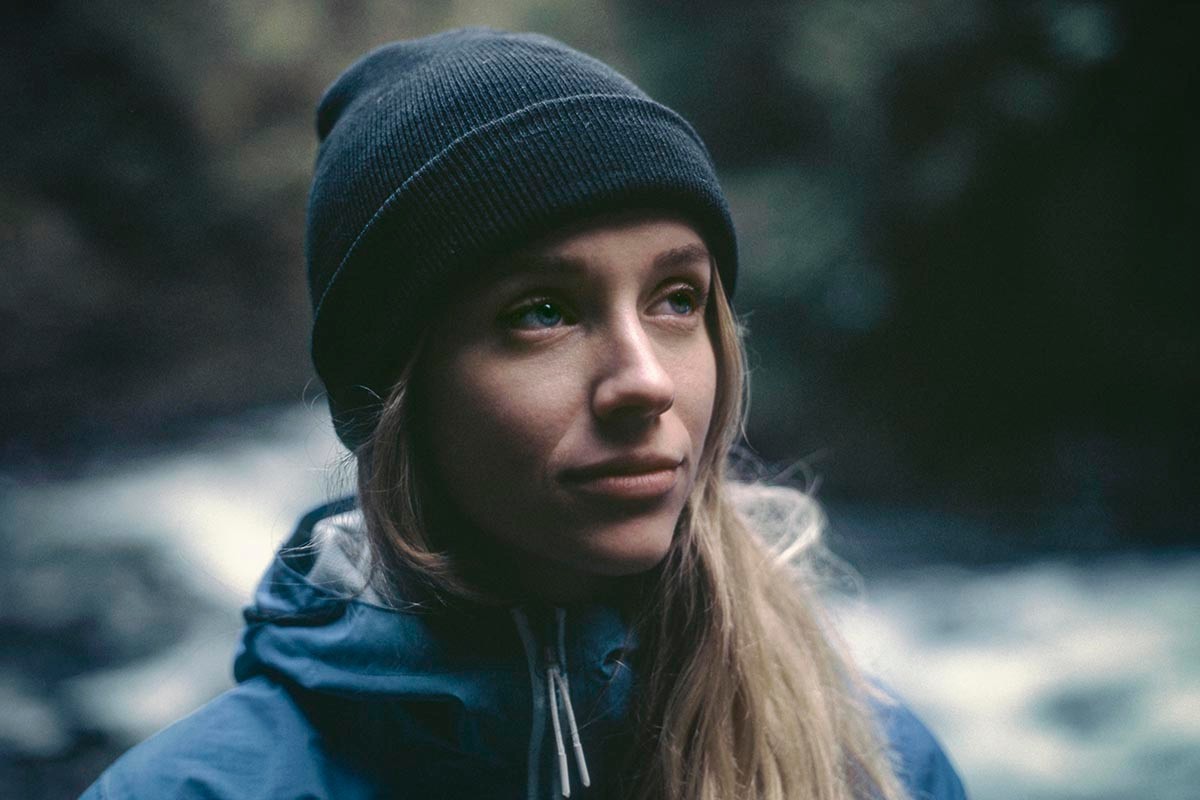 A young blonde person looking to the right wearing a toque in the wilderness