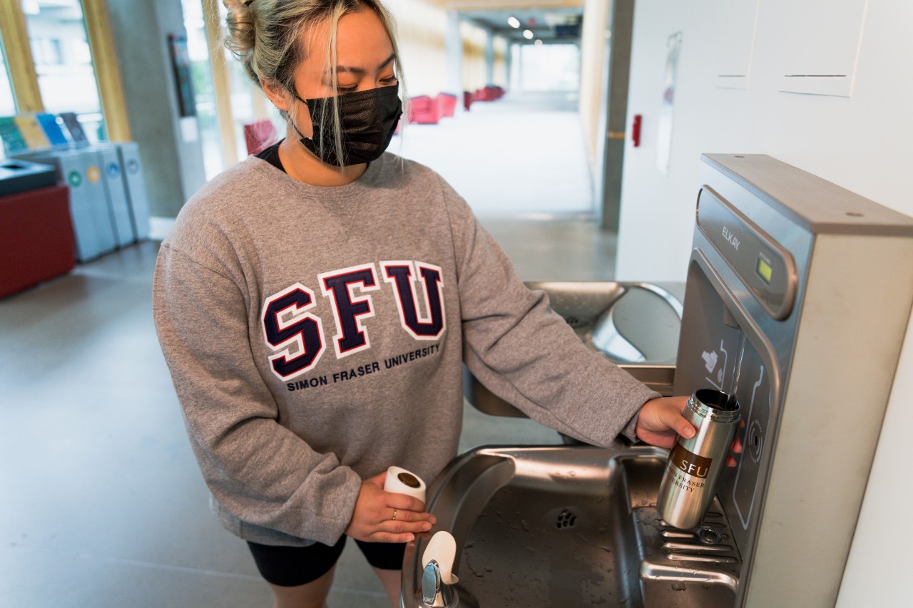 Student standing at a water filling station filling a reusable bottle
