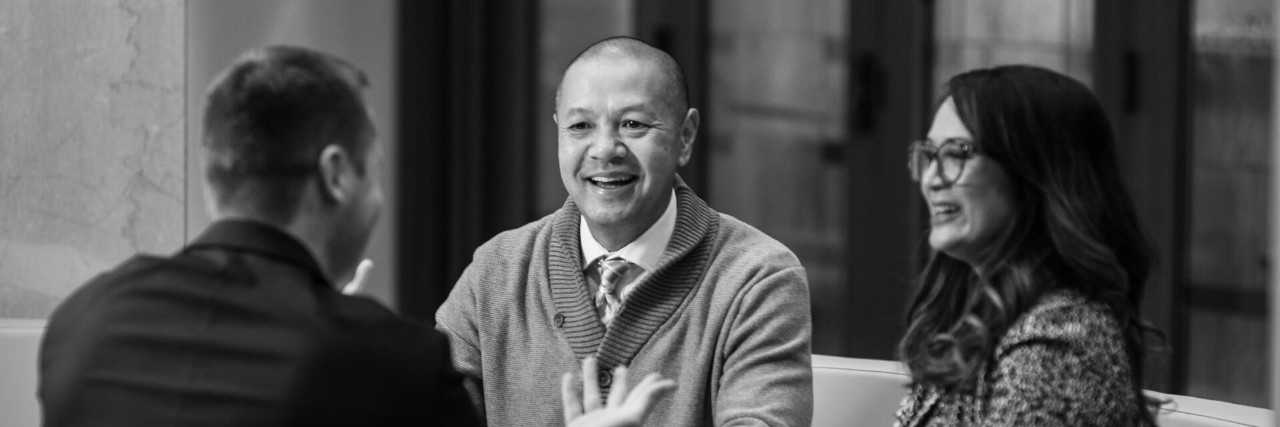 Three middle-aged professionals sitting together and having a conversation in an indoor meeting space.