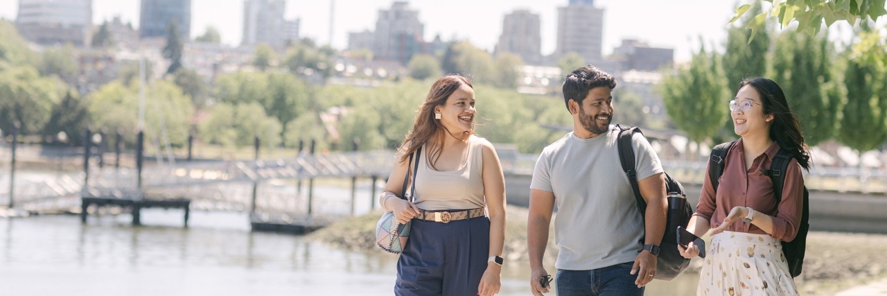 Three SFU Beedie students walking and chatting outdoors on a sunny day.