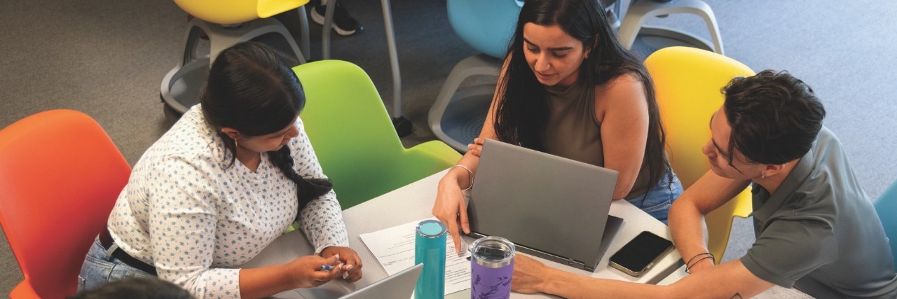 Three SFU Beedie students working together around a laptop in a study space.