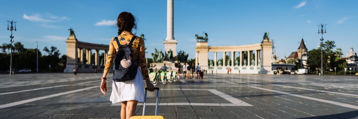 A student walking with a suitcase in a large open plaza.