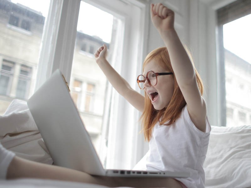 Little girl looking happily at computer with hands up
