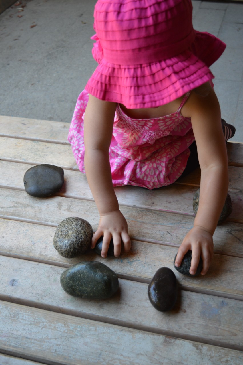 Child in pink hat and dress playing with rocks