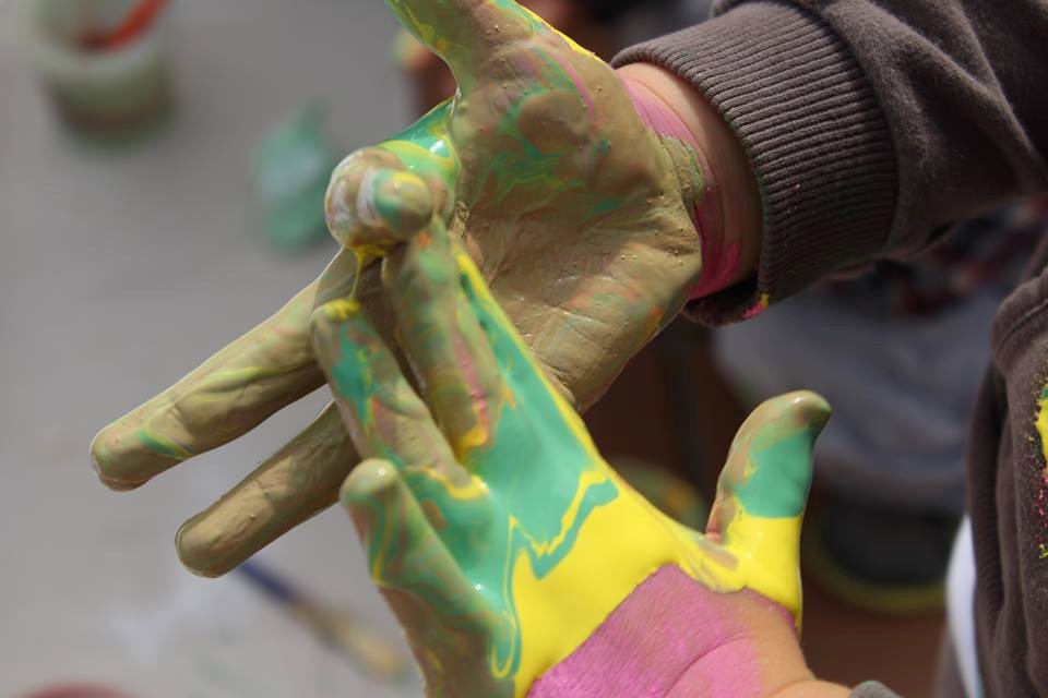 A child's hands with green and yellow paint smeared on them