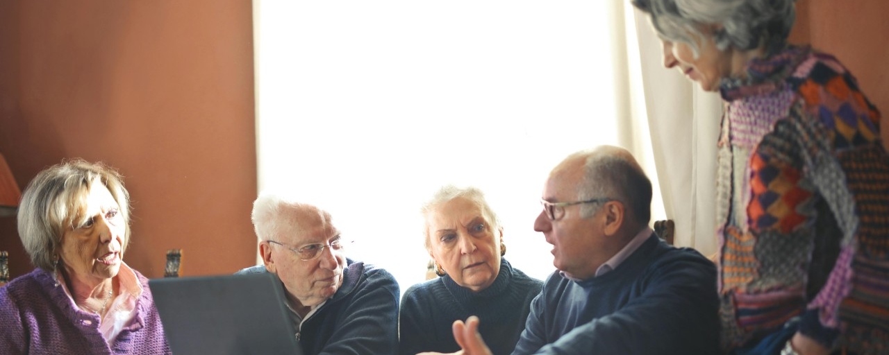 A group of five older adults engaging in a discussion with a laptop infront of them