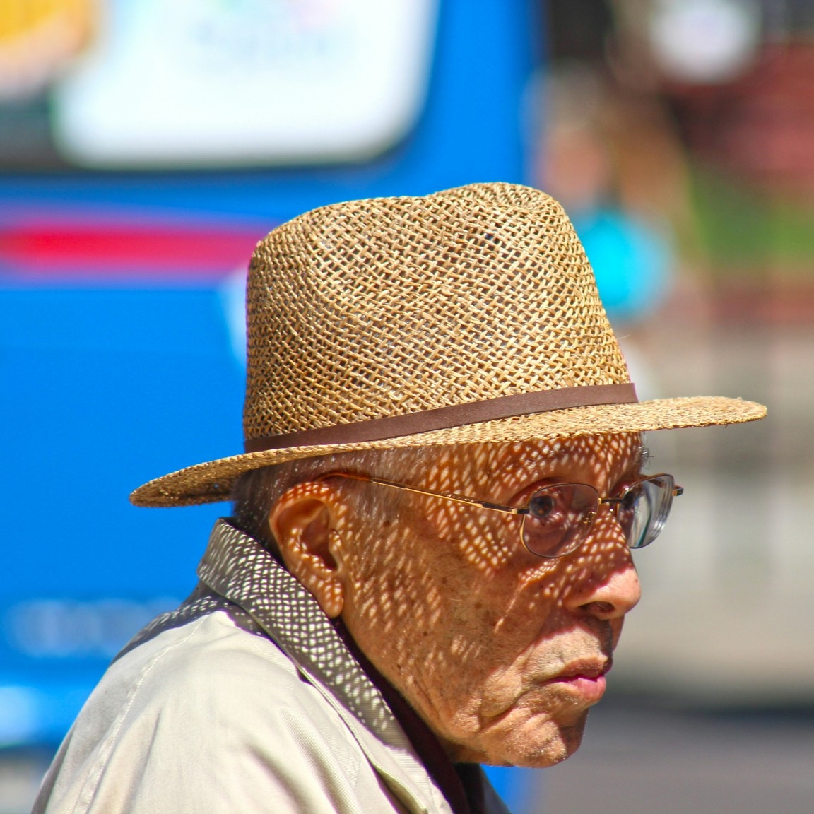 Older adult male wearing a straw hat on a sunny day, showing patterned shadow on his face