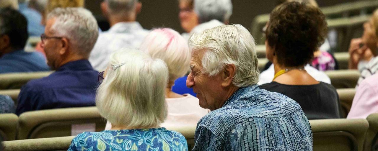 View from the backside of an older couple attending a conference, discussing among themselves.