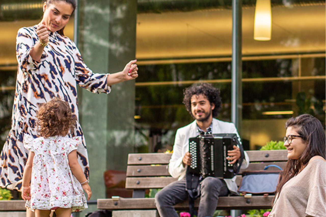 Toddler and parent dancing while person plays accordion on public bench