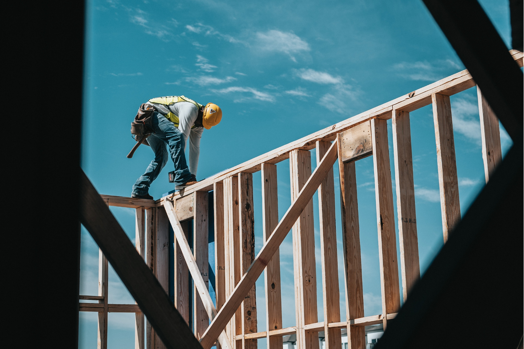 Construction worker standing on wooden framing outdoors with a blue sky background