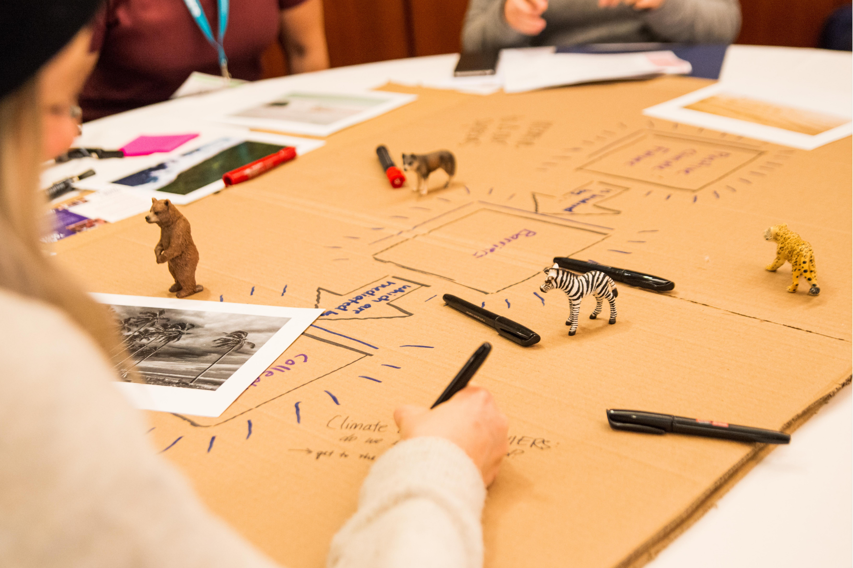 People drawing on brown paper and toy animals placed on table