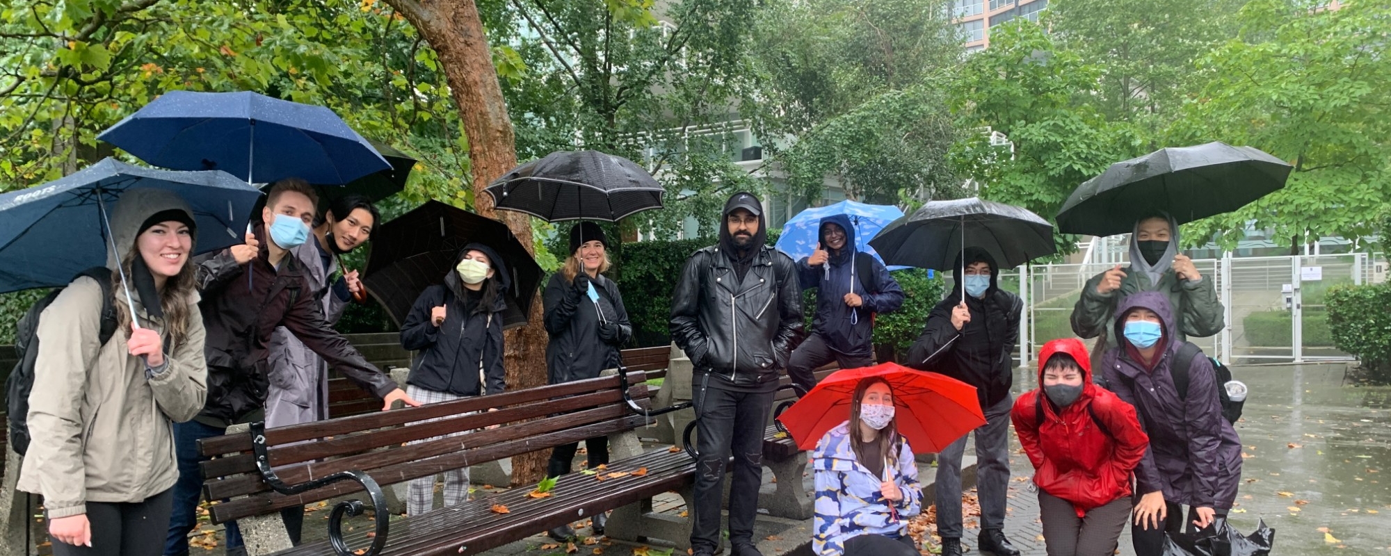 Fall 2021 Semester by the Salish Sea students standing outside behind a bench, it is raining and several students have open umbrellas