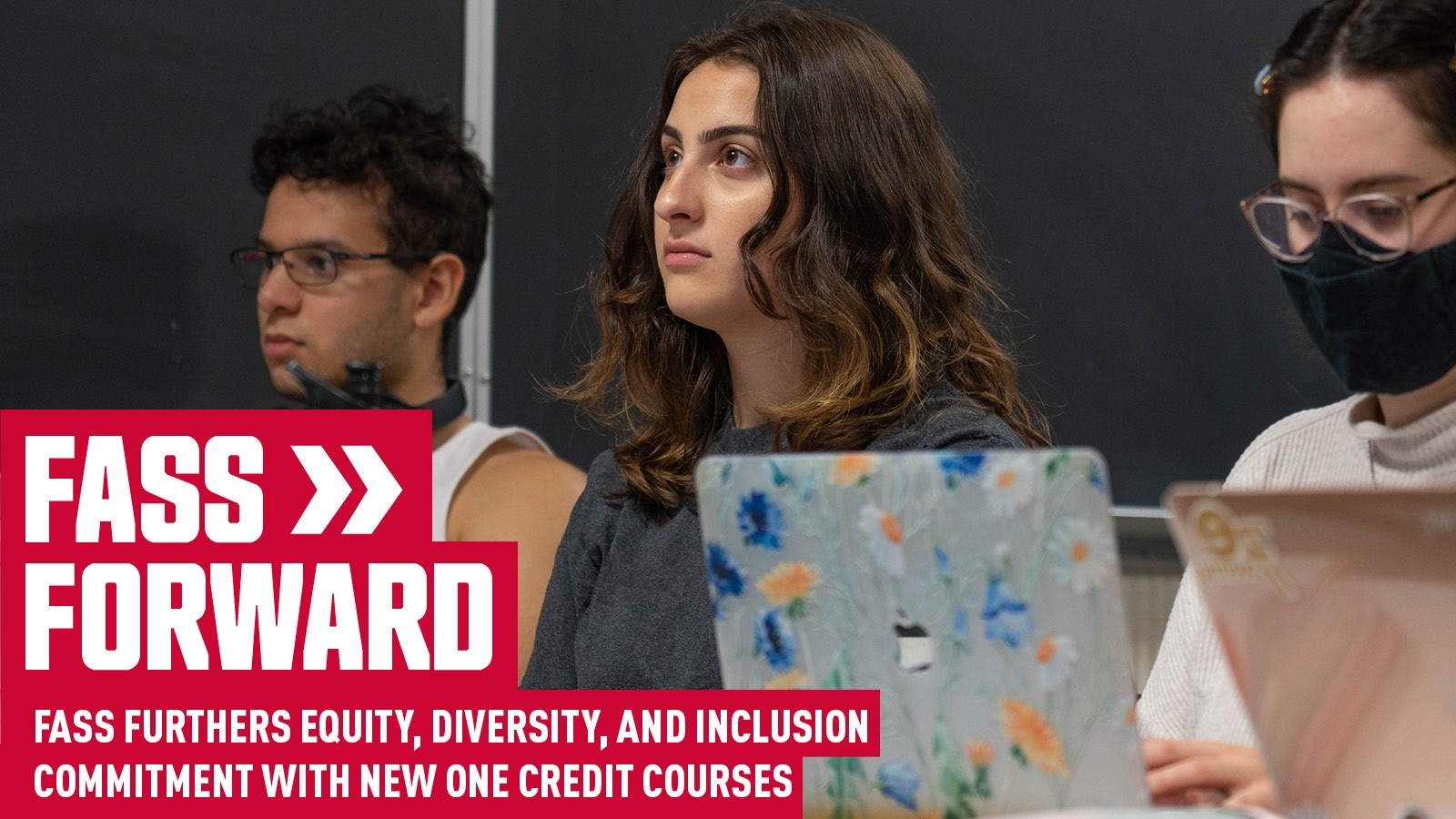 Three students sit in a classroom as they watch a presentation. Their laptops are open in front of them. The student is the middle who is the focus of the image is female presenting with dark brown wavy hair and a grey shirt. In the bottom left corner is white text on a red background that reads: FASS >> FORWARD FASS FURTHERS EQUITY, DIVERSITY, AND INCLUSION COMMITMENT WITH NEW ONE CREDIT COURSES