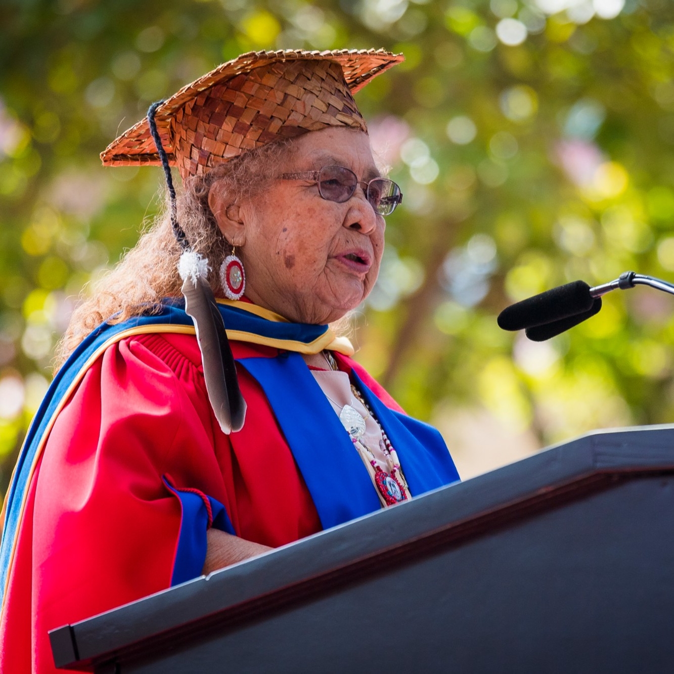 Ruby Peters is photographed giving a speech at the 2021 Convocation ceremony. She wears graduation regalia along with a cedar graduation cap.