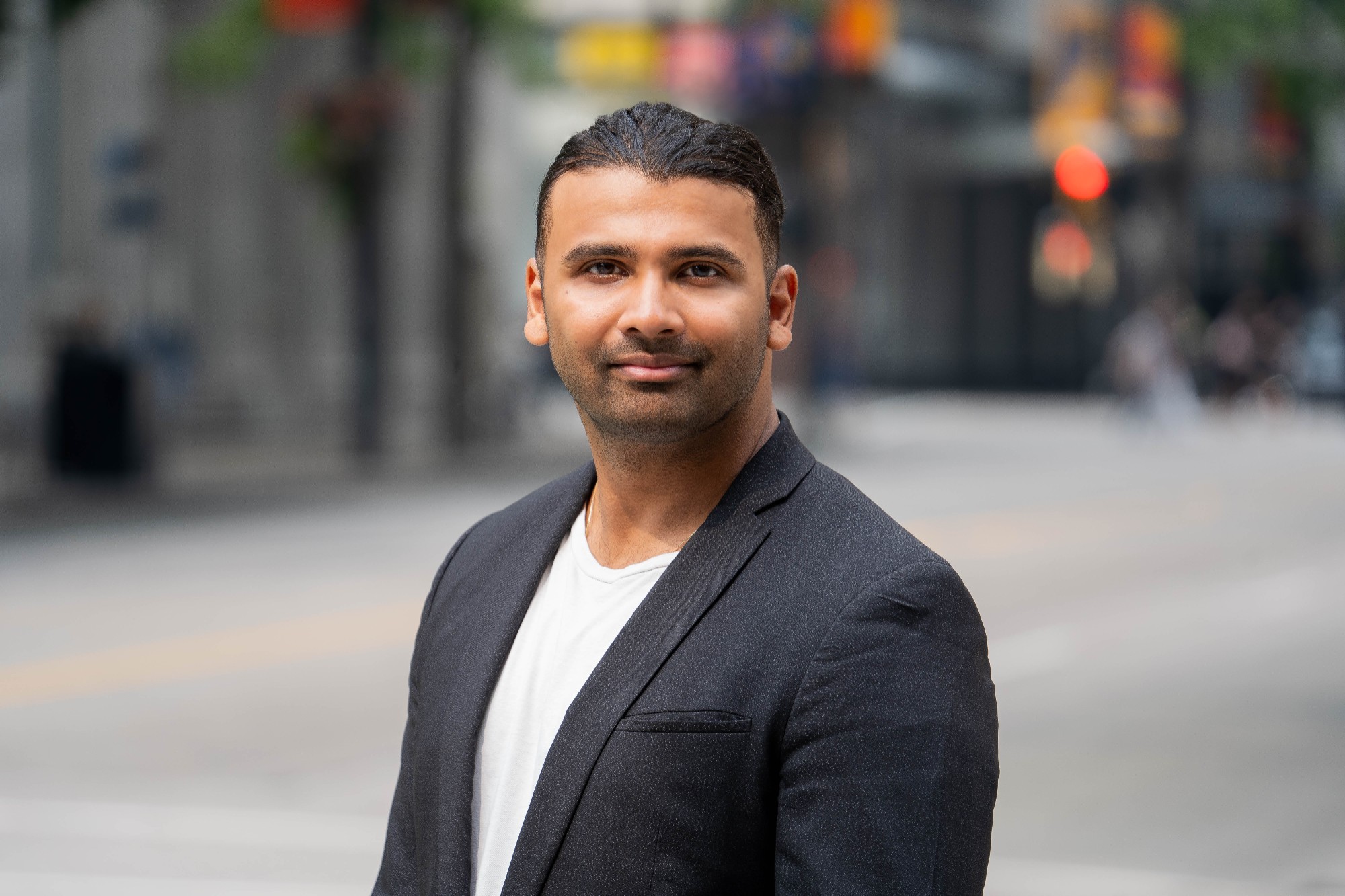 Portrait of Dr. Ali Bhagat, Director of SFU School of Public Policy Minor, with a background of an urban street.