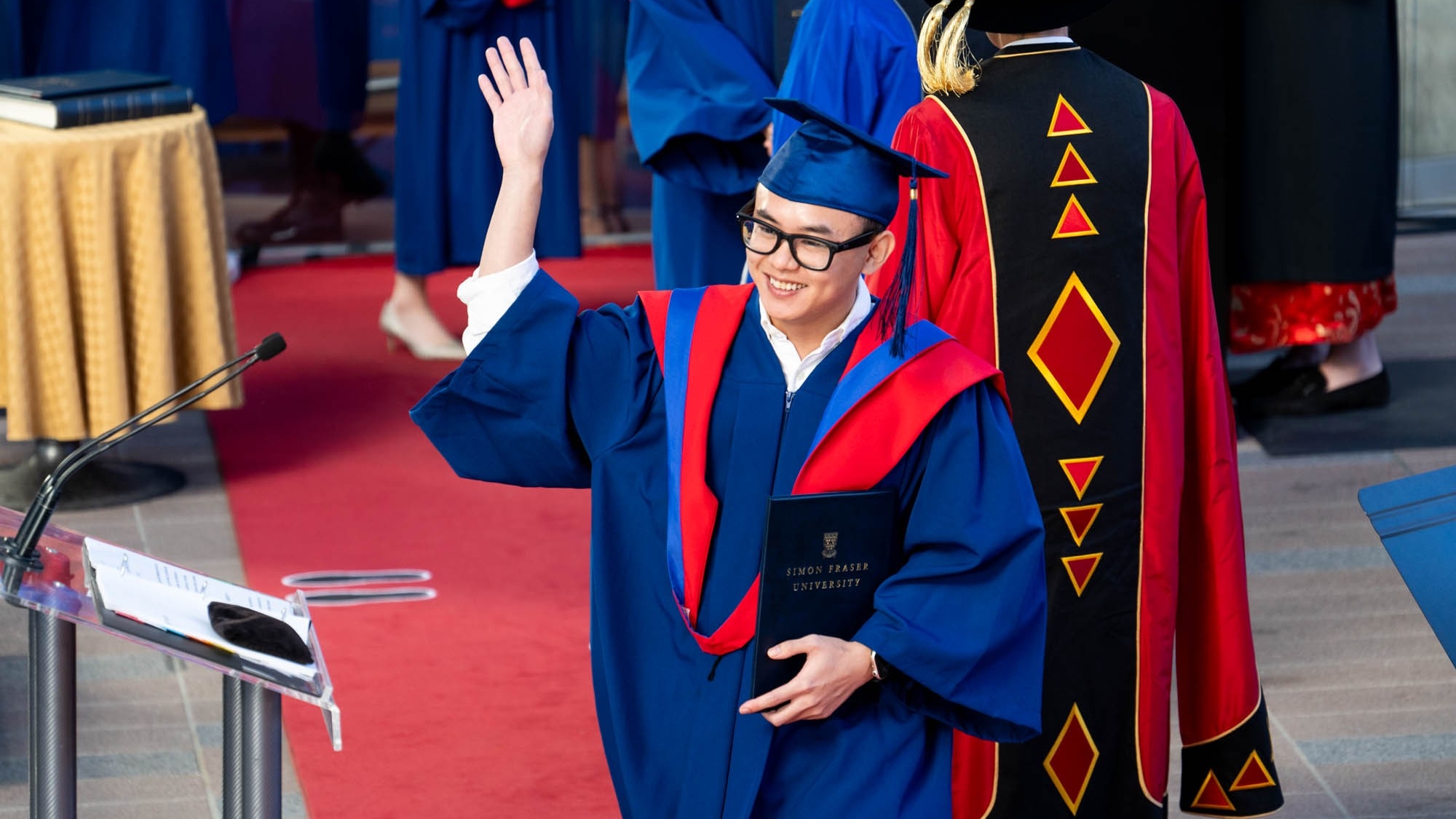 A FASS graduate crosses the stage at Convocation waving to the audience.